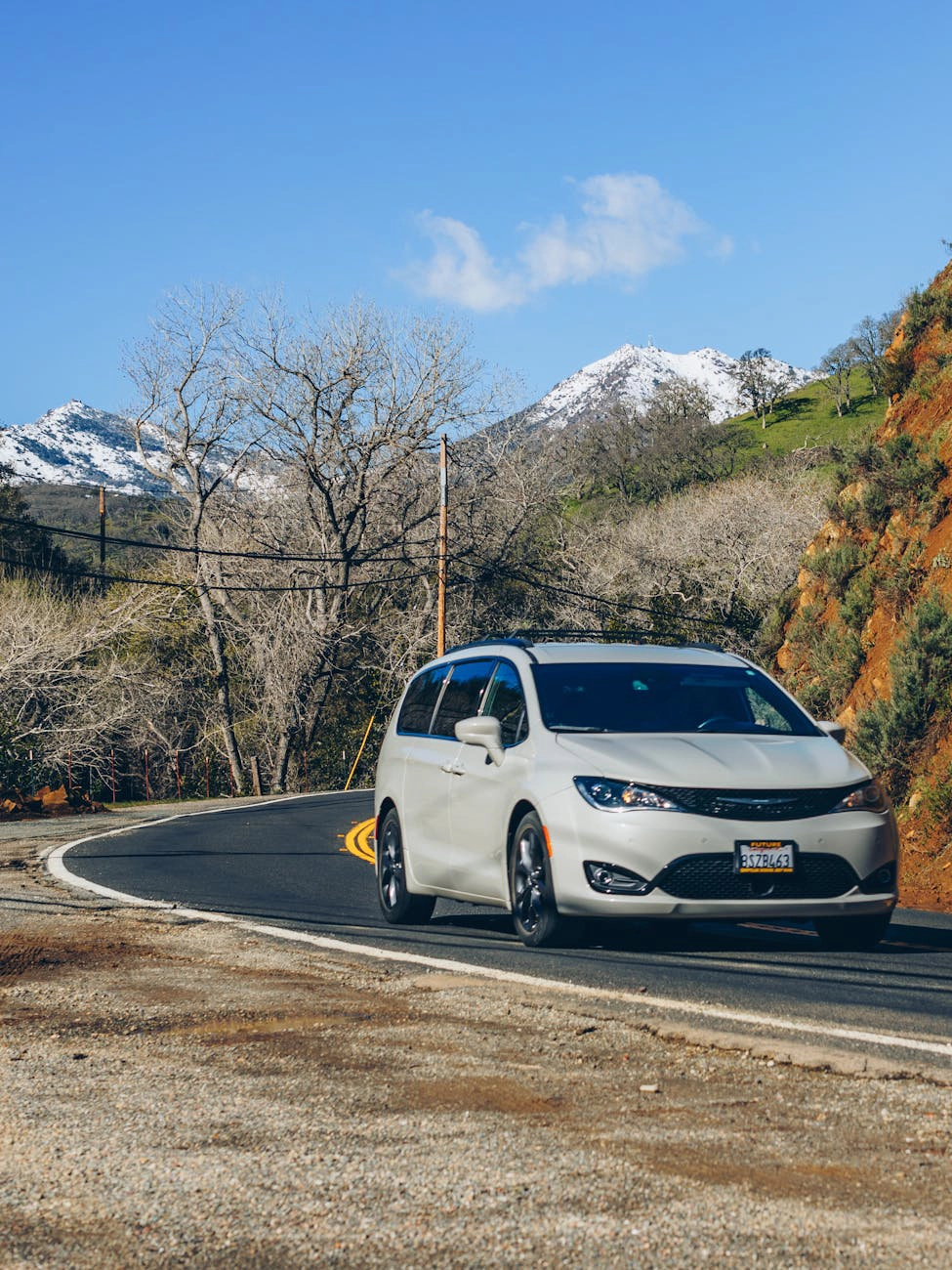 A white passenger minivan driving on a mountain road.