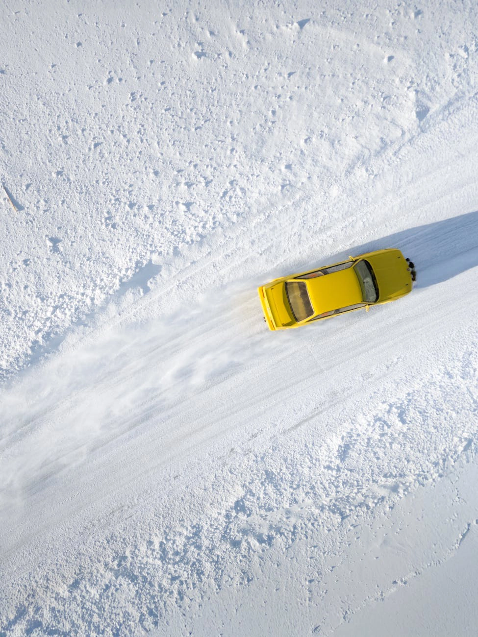 A yellow car driving on a snow-covered road.